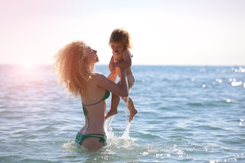 Mother in bikini standing swimming and playing with her child in the sea