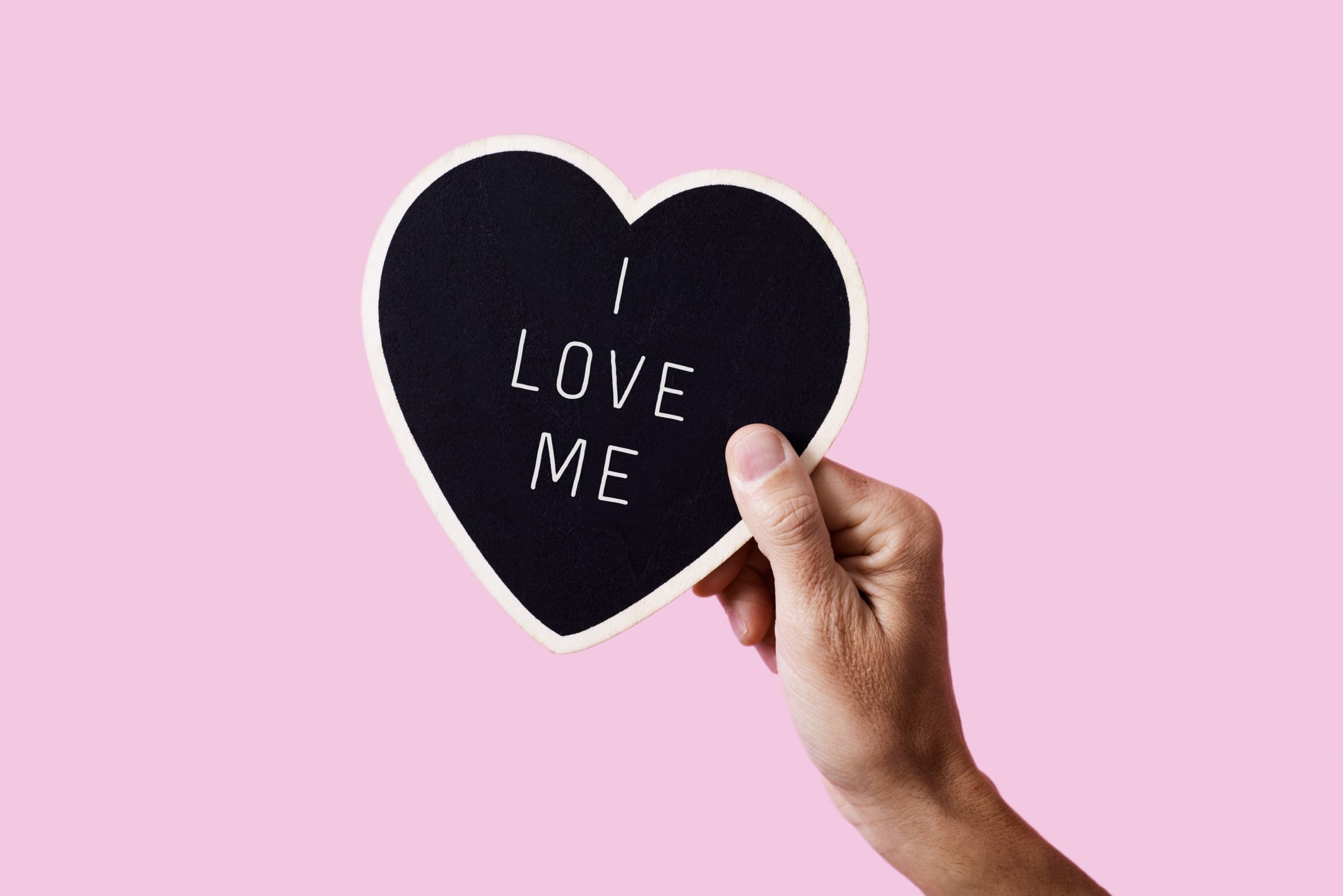 Hand holding paper heart with "I Love Me" printed on it